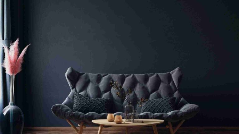 Dark minimalist living room with a tufted gray sofa, round wooden coffee table, and a vase of pink pampas grass on the left