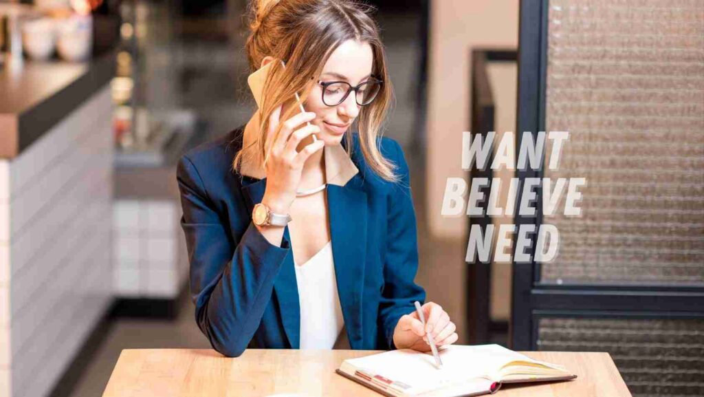 A woman in a blue blazer sits at a table in a cafe, talking on a mobile phone while writing in a notebook. Text on the image reads 'WANT BELIEVE NEED'.