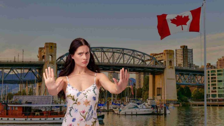 Woman in a floral dress raises both hands in front of a marina, with boats, a bridge, and a waving Canadian flag nearby.