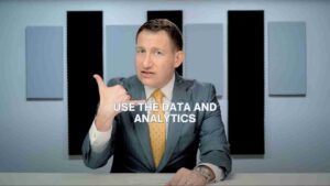 Man in a gray suit at a desk giving a thumbs-up, with the caption 'USE THE DATA AND ANALYTICS' across the center of the image.