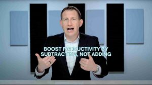 Man in a suit speaks at a desk with the caption: 'Boost productivity by subtracting, not adding'.