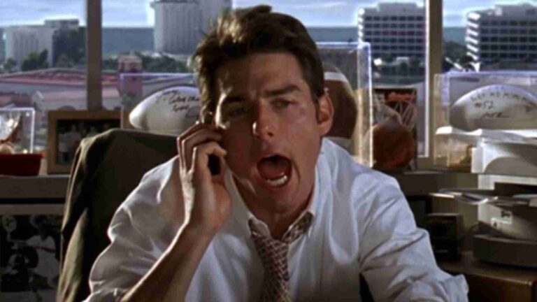 Businessman in a white shirt and tie on a phone call, shouting or speaking loudly in an office setting with cityscape outside