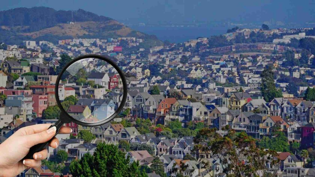 Hand holding a magnifying glass over a densely packed suburban neighborhood