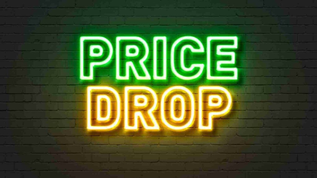 Neon sign on a brick wall reading 'PRICE DROP' in green for PRICE and yellow for DROP.