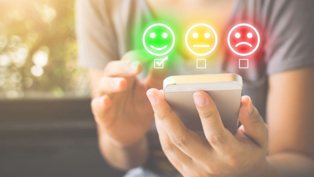 Person holding a smartphone with three mood icons above him: green happy, yellow neutral, red sad, symbolizing feedback options