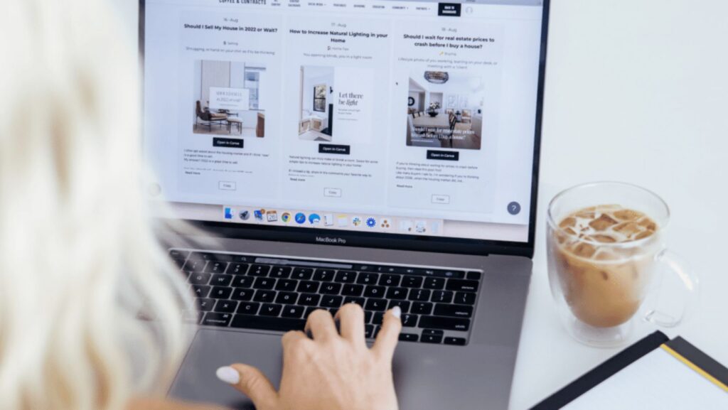 Person typing on a MacBook Pro with a three-column website layout on screen; iced coffee beside.