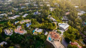 Aerial view of a hillside suburb with large houses, winding roads and many trees with pool-filled backyards nearby.