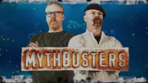 Two men stand side by side behind a banner reading 'MYTHBUSTERS' against a blue backdrop, arms crossed or relaxed pose.