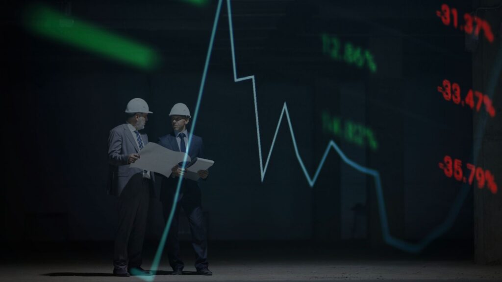 Two men in suits and hard hats examine blueprints in a dark room with a glowing stock-market line chart behind them.