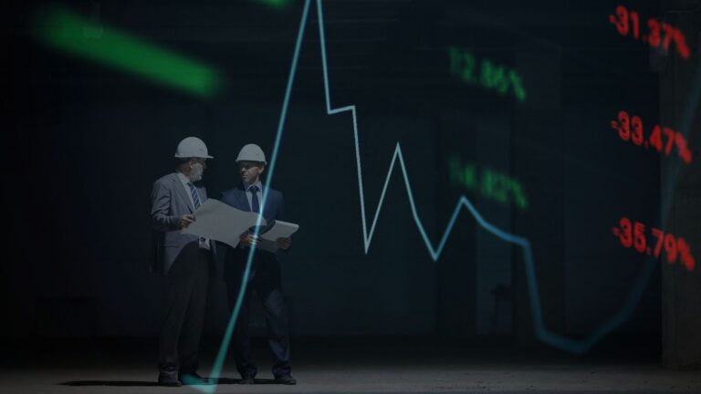 Two men in suits and hard hats examine blueprints in a dark room with a glowing stock-market line chart behind them.