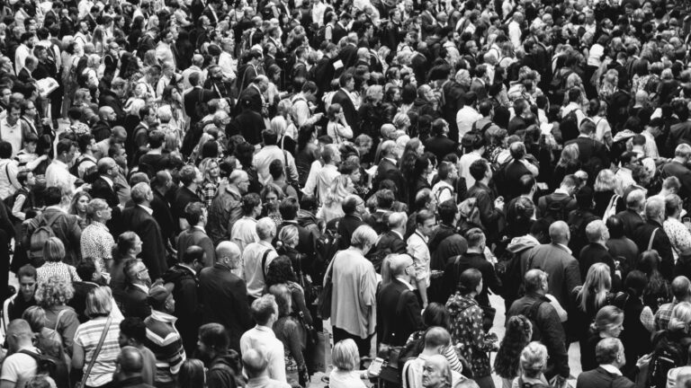 Dense crowd of people standing closely together in a public space (black and white photo).