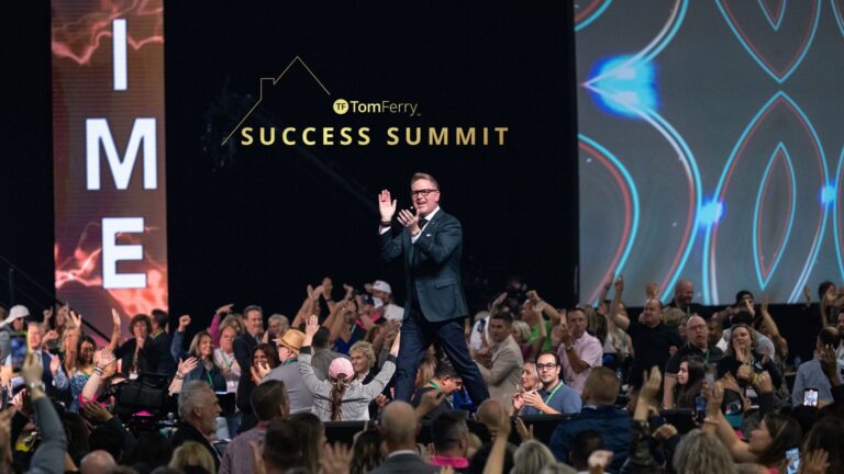 Speaker on stage at a Success Summit, with Tom Ferry logo and 'SUCCESS SUMMIT' on backdrop; audience cheers in the foreground.
