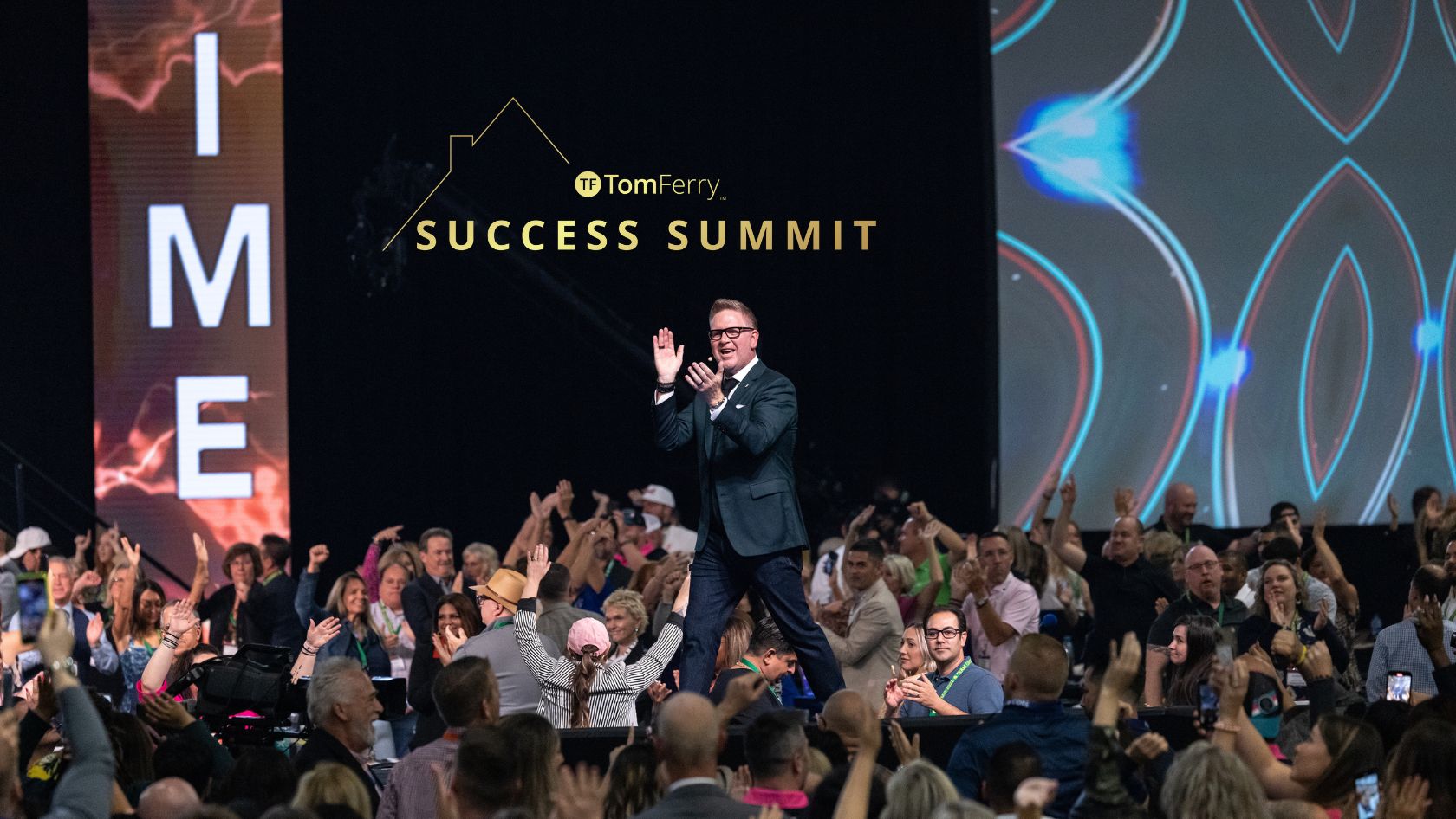 Speaker on stage at a Success Summit, with Tom Ferry logo and 'SUCCESS SUMMIT' on backdrop; audience cheers in the foreground.