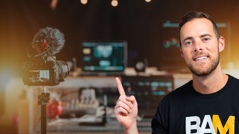 Smiling man in a black BAM shirt points at a DSLR on a tripod in a recording studio with a blurred workstation in the background.