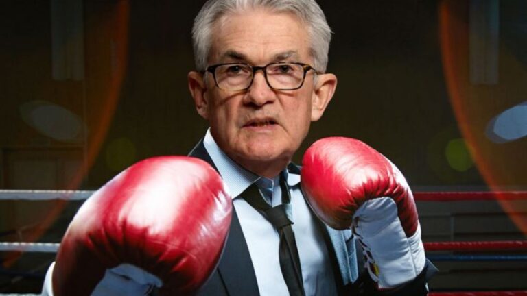 Older man in a suit and tie wearing red boxing gloves, standing in a boxing ring as if ready to fight.