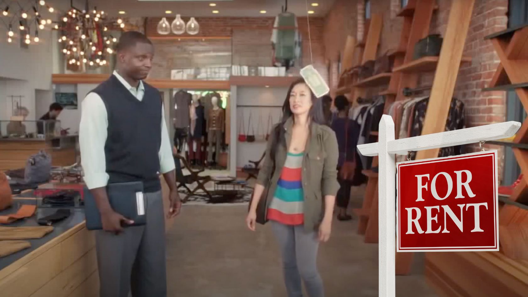 Man in a vest and shirt holds a tablet/ notebook inside a clothing store while a woman in a striped top walks beside; a 'FOR RENT' sign hangs in the foreground.