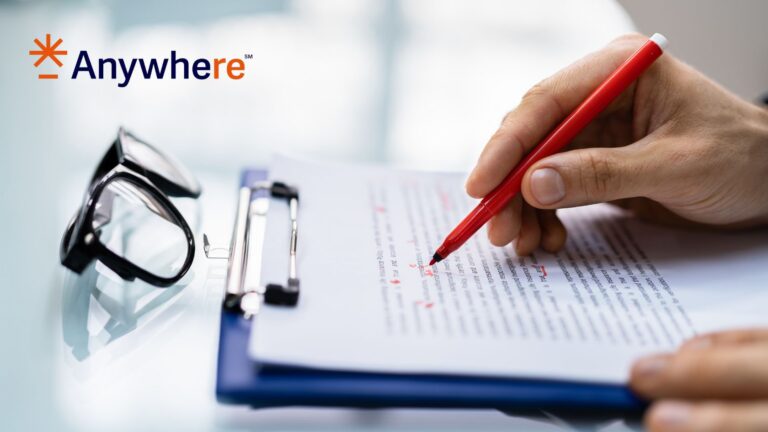 Hand signing a contract with a red pen on a clipboard; glasses sit nearby with the Anywhere logo in the top left corner.