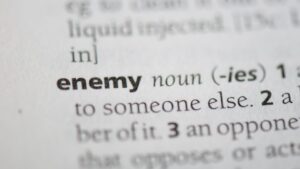 Close-up of a dictionary entry for the noun 'enemy' with the definition text visible nearby.