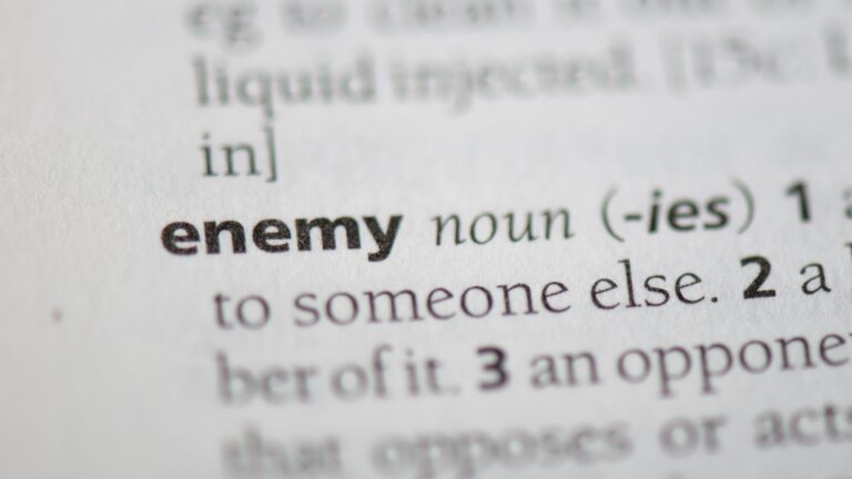 Close-up of a dictionary entry for the noun 'enemy' with the definition text visible nearby.