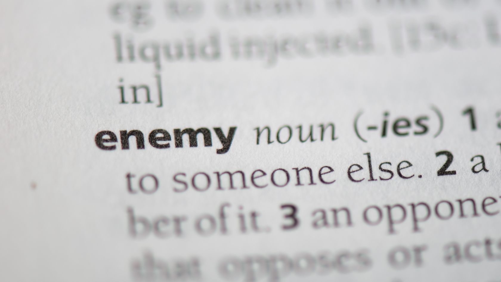 Close-up of a dictionary entry for the noun 'enemy' with the definition text visible nearby.