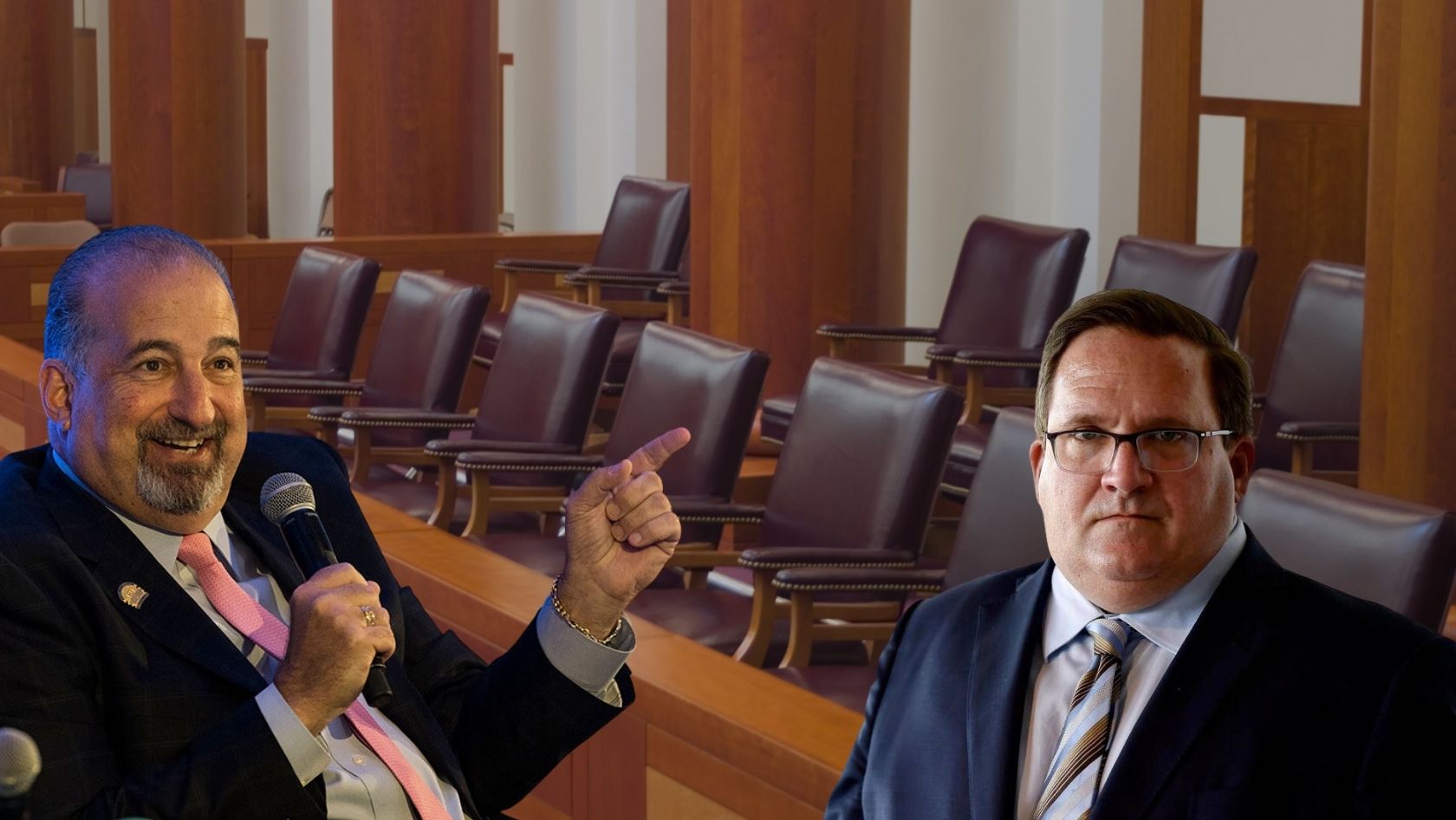 Two men in suits sit in a wood-paneled hearing room; one holds a microphone and points as he speaks, the other listens nearby in glasses.