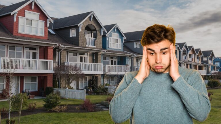 Young man holding his temples in distress in front of a row of colorful suburban townhouses in an outdoor scene.