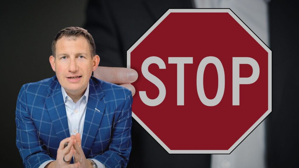 Man in a blue checkered suit sits with hands clasped beside a large red stop sign graphic