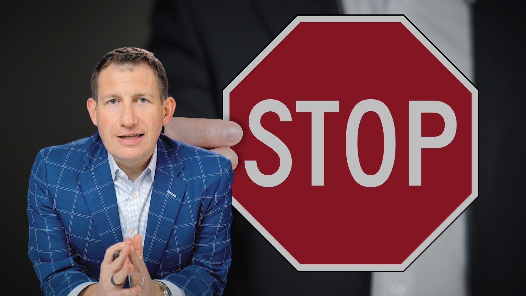 Man in a blue checkered suit sits with hands clasped beside a large red stop sign graphic