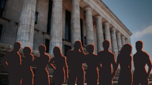 Group of silhouetted people standing on stone steps in front of a neoclassical building with tall columns.
