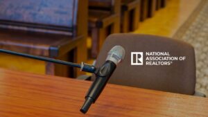 Microphone mounted on a stand over a wooden table in a meeting room, next to a brown chair with the National Association of Realtors logo visible on it.
