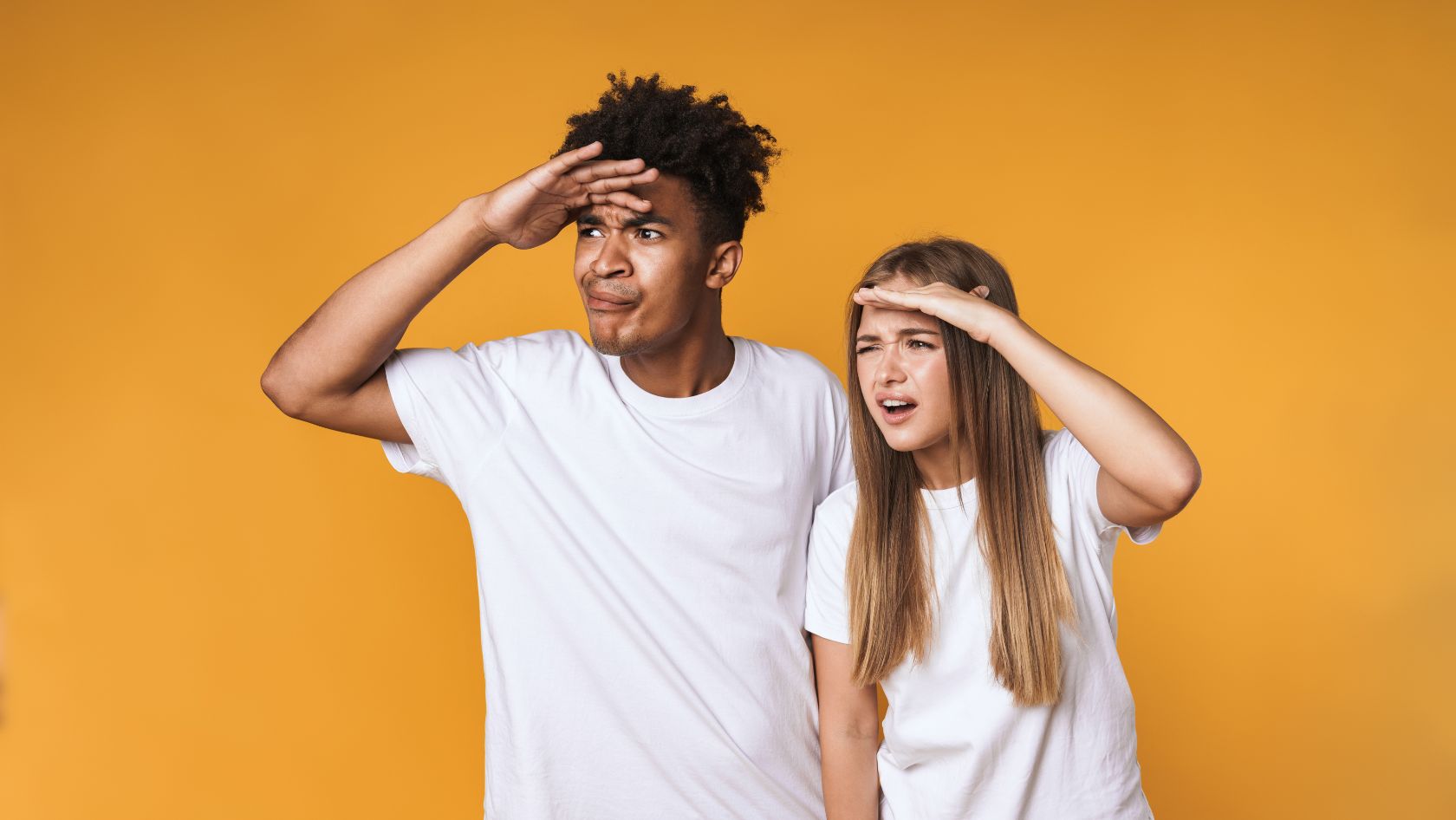 Two young people in white shirts shielding their eyes as they look into the distance against an orange background