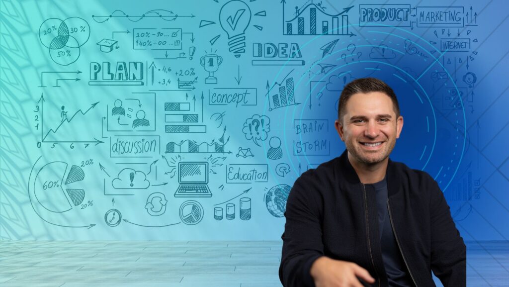 Smiling man in a dark jacket sits in front of a wall covered with hand-drawn business diagrams, charts and ideas in blue tones.