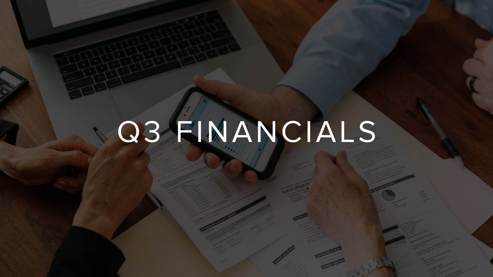 Meeting scene with hands reviewing financial documents and a smartphone on a wooden table, overlaid with 'Q3 FINANCIALS' text.