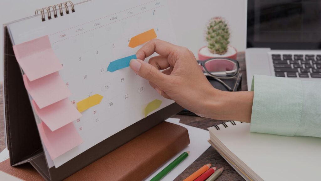 Person placing blue and orange sticky notes on a desk calendar while planning.