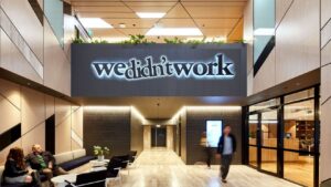 Modern office lobby with a large glowing sign reading 'we didn’t work' above a hallway; people seated on the left and a blurred man walking by.