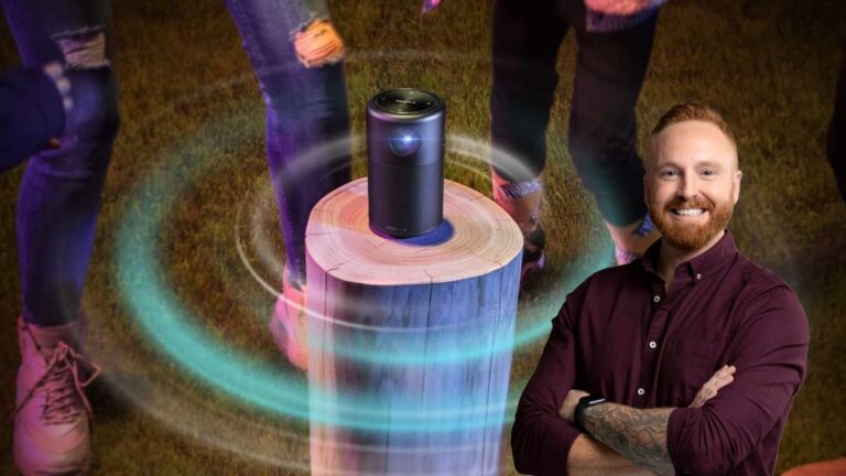 Smiling man with folded arms beside a portable speaker on a tree stump, surrounded by colorful light rings and silhouettes of people in the background.