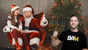 Festive scene: Santa sits in a chair with a girl on his lap, while a man in a BAM shirt holds a menorah beside a Christmas tree.