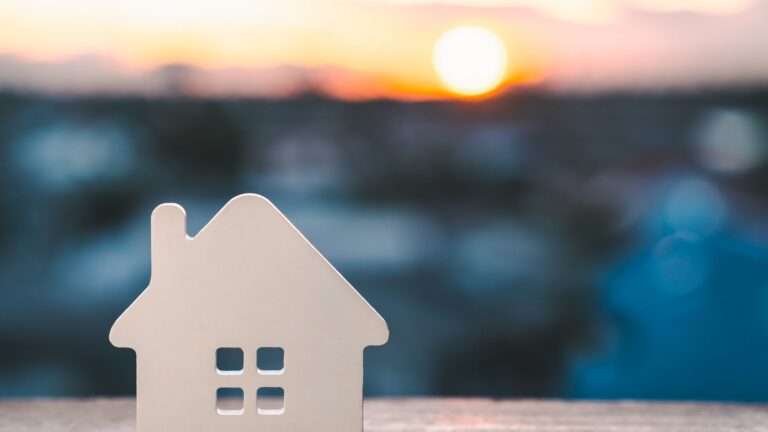 A white, cutout house silhouette with windows in the foreground at sunset.
