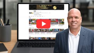 Man in a blue check blazer sits beside an open laptop showing a YouTube channel page with a large red play button overlay and video thumbnails in the center area.