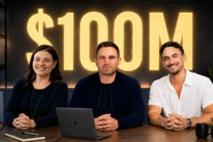 BAM_Webinar_How_to_Build_a_100M_Real_Estate_Team - BAM Three people sit at a table in front of a large glowing $100M sign in a studio setting with a laptop and notebook on the table.